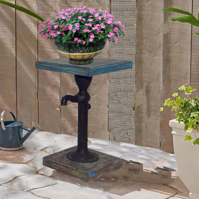Hand pump plant stand with a potted flower on a patio.