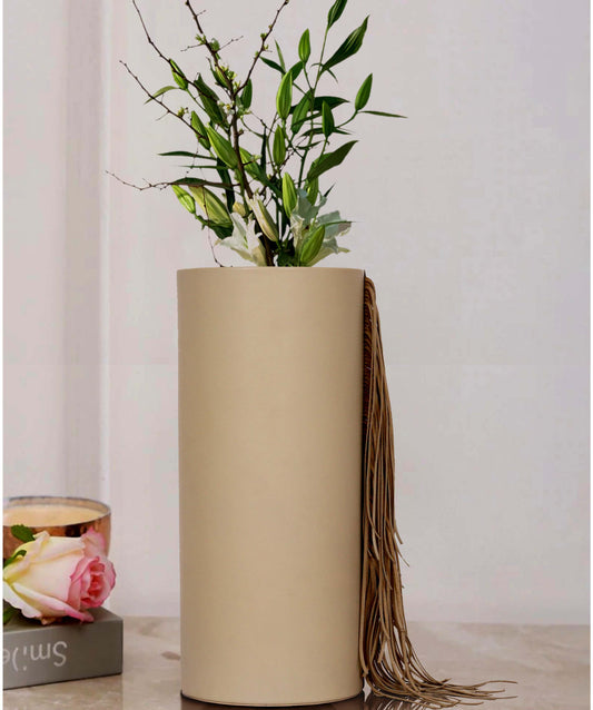 Tall cream leather vase with stylish fringes and green plant.